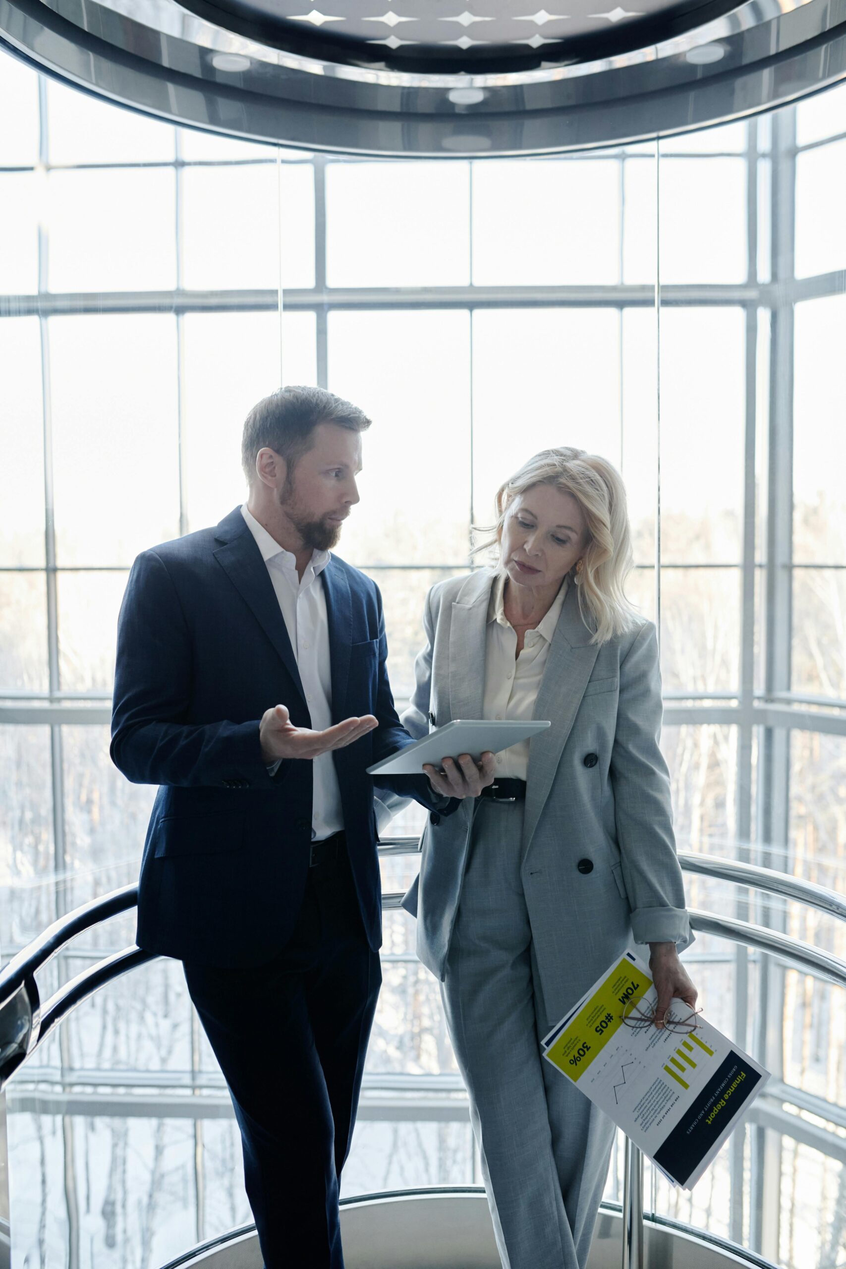 Business professionals in a modern office setting discussing work with digital tablet and documents.